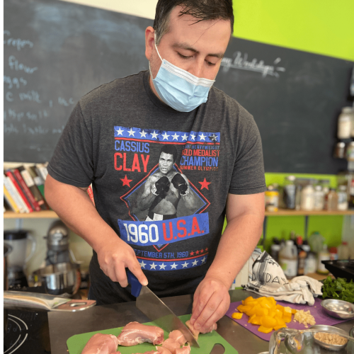 man with a mask on cutting raw chicken in a kitchen