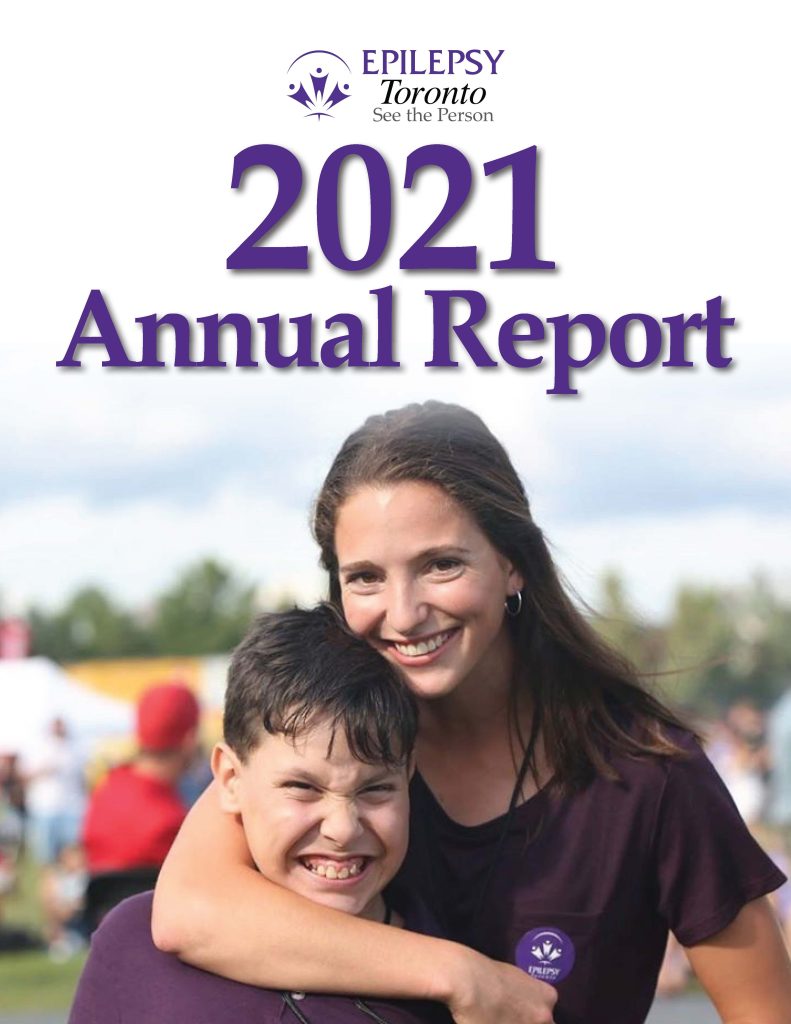Boy smiles widely as smiling woman stands behind him with arm affectionately around him. They are outside and are both dressed in purple t-shirts. She has an Epilepsy Toronto sticker on her shirt.