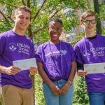 Three people wearing Epilepsy Toronto Purple Shirts stand smiling, the two on the ends each hold a certificate in front of them.